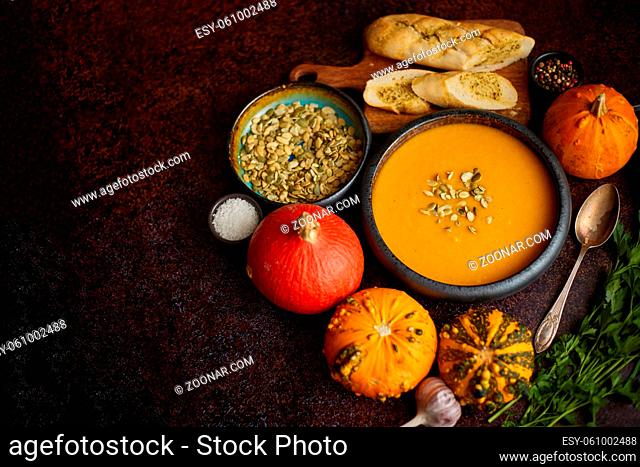 Homemade vegetarian pumpkin cream soup served in ceramic bowl. Decorated with seeds. Various ingredients on side. Top view, flat lay