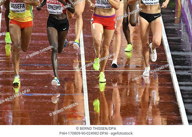 The legs of the runners in the first heat of the women's 3000 metres hurdles are reflected in the tartan track, which is wet with rain