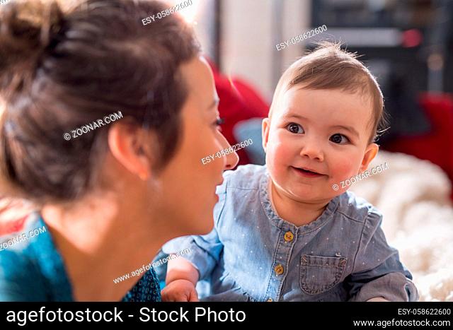 Mother is playing with her cheerful baby on the couch at home