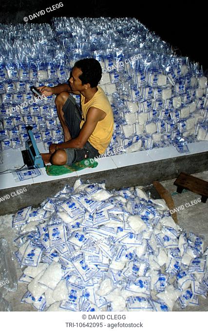 Young man surrounded by clear plastic packets of salt checks his mobile phone in a small salt iodizing business Sakra Lombok Timur NTB Indonesia