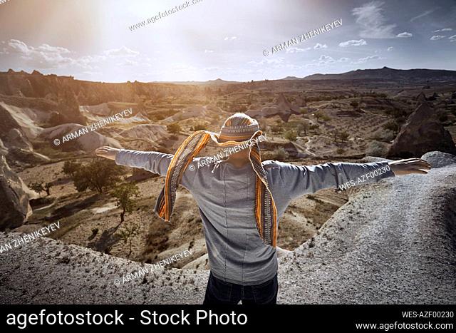 Male tourist with arms outstretched standing on rock in Cappadocia during sunny day, Turkey