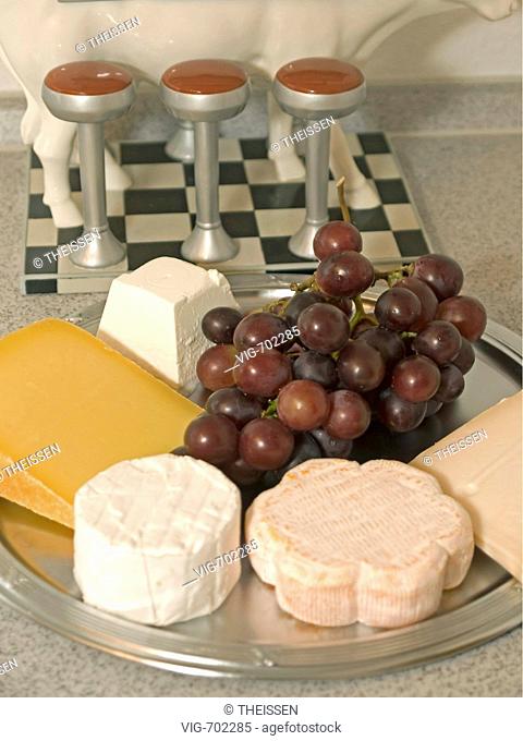 different kind of cheese with grapes on a plate in kitchen, funny figure of a cow bar in the background as decoration. - 31/12/2007