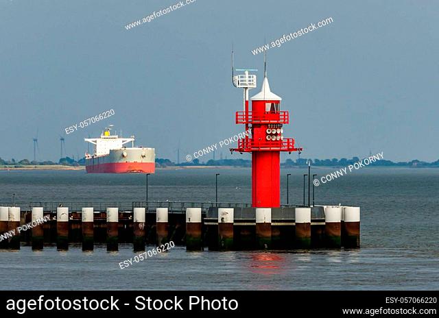 Red lighthouse Mole 2 at the Brunsbuettel lock with cargo ship in background, Schleswig-Holstein, North Sea, Germany