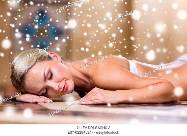 people, beauty, spa, healthy lifestyle and relaxation concept - beautiful young woman lying on hammam table in turkish bath with snow effect