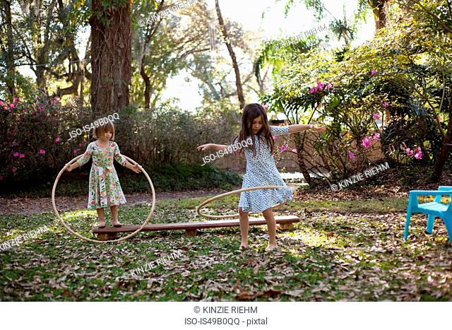 Two sisters playing with plastic hoops in shaded garden