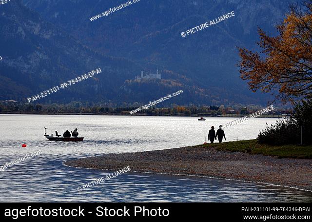 01 November 2023, Bavaria, Roßhaupten: Day trippers enjoy the sunny weather on the shores of Lake Forggensee, located below Neuschwanstein Castle