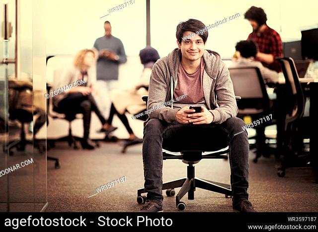 young indian male software developer using mobile phone writing messages while having break at modern creative startup office