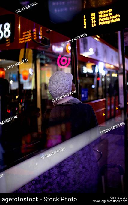 Mujer joven con sombrero esperando el autobús de la ciudad por la noche, Londres, Reino Unido