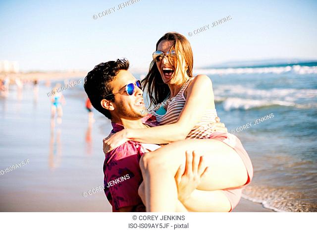 Young man carrying girlfriend on beach, Santa Monica, California, USA