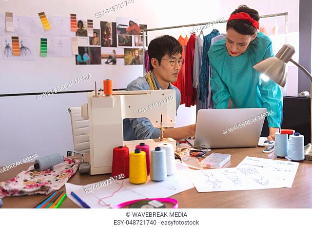 Fashion designers discussing over laptop at desk in design studio