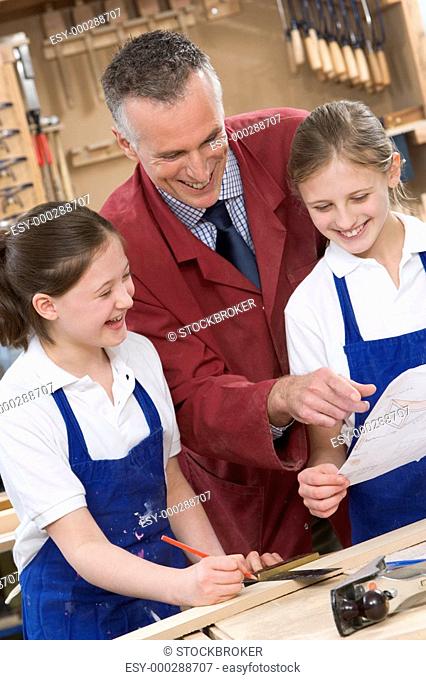 Female students reviewing woodworking plans with teacher