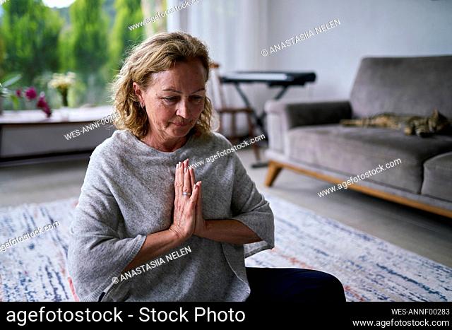 Senior woman with hands clasped practicing yoga at home