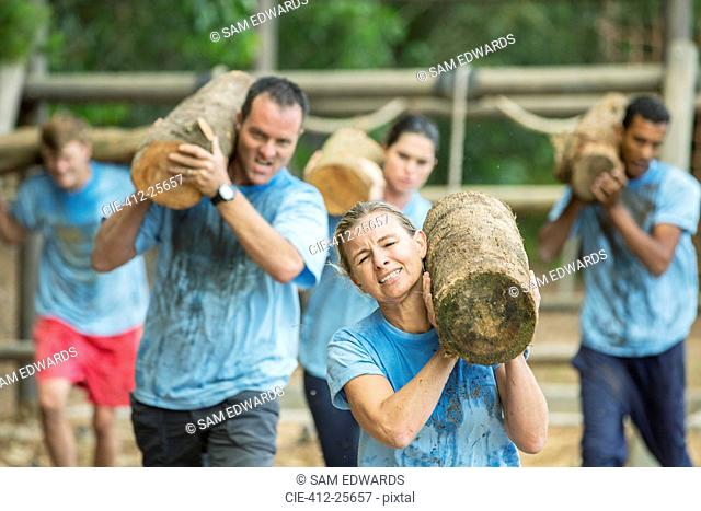 Determined people running with logs on boot camp obstacle course