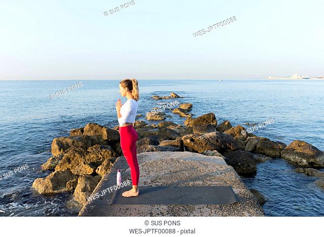 Young woman practicing yoga on the beach, doing prayer position
