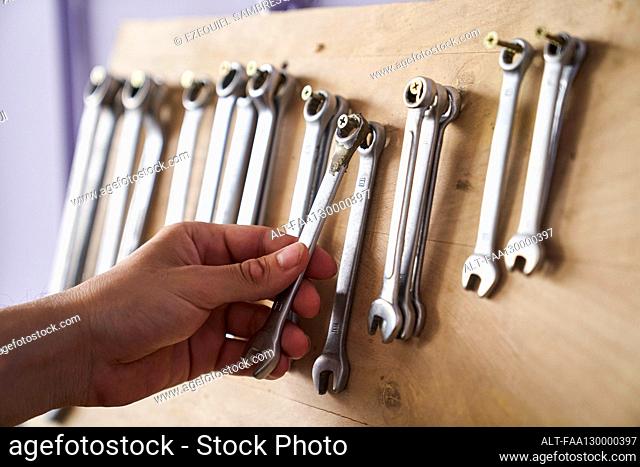 Close-up shot of hand taking a combination spanner from a wall rack