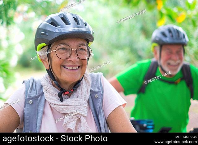 Portrait of one old woman smiling and enjoying nature outdoors riding bike with her husband laughing. Headshot of mature female with glasses feeling healthy