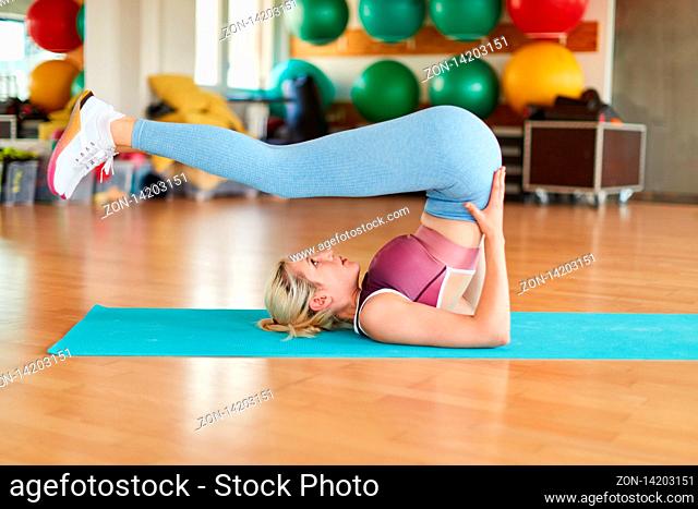 Junge Frau macht einen Schulterstand auf der Matte im Yoga Kurs