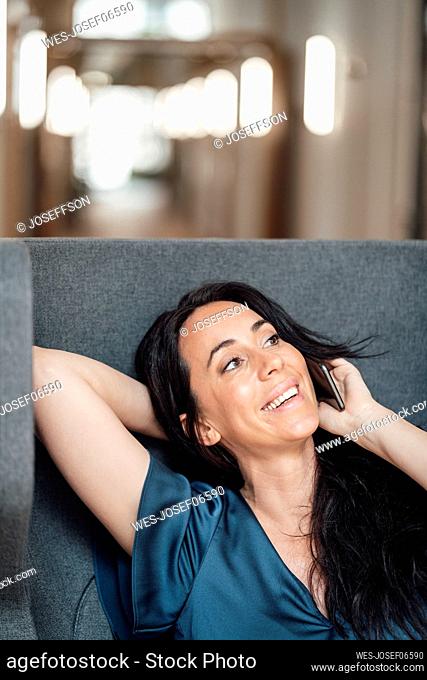 Smiling businesswoman talking on mobile phone sitting on armchair in office