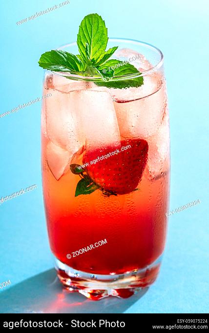 Glass of strawberry drink with ice cubes and mint leaves on a seamless blue background. A single glass of fruity cocktail. Summer sweet drink