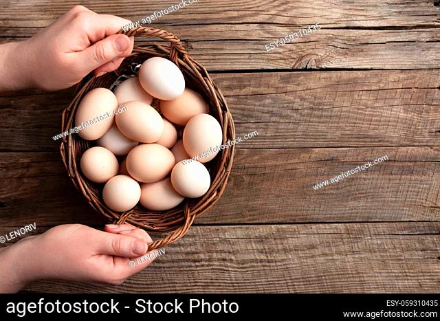 Flat lay with hands holding basket with organic chicken eggs on wooden background. Organic household concept with eggs from free-range and pasture raised hens