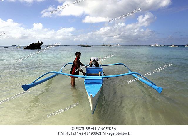 09 December 2018, Philippines, Boracay: Two men repair a typical Philippine boat on the beach. The beaches of the island of Boracay were closed to the public...