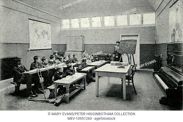 Lord Mayor Treloar Cripples' Home, Alton, Hampshire. In winter, lessons were conducted indoors. This classroom has a female teacher next to a blackboard