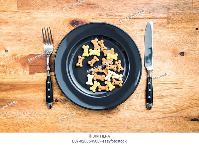 Dog food shaped like bones on plate and cuttlery. Top view