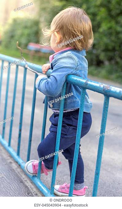Sadly bored little girl in the park rest on railing