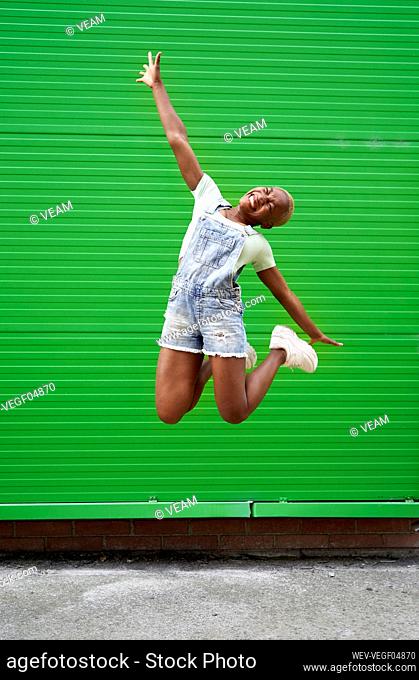 Excited woman jumping in front of green wall