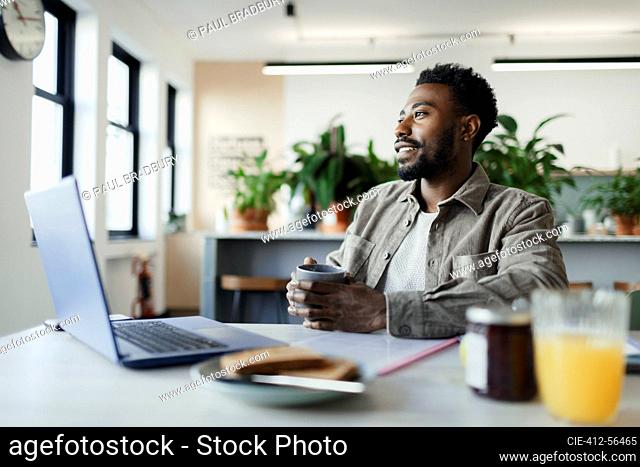 Thoughtful businessman with coffee working at laptop in office