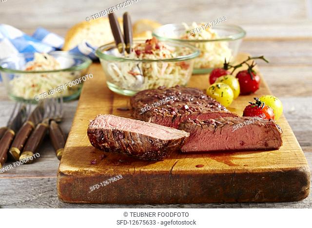 A medium grilled flank steak with coleslaw and cherry tomatoes on a wooden board