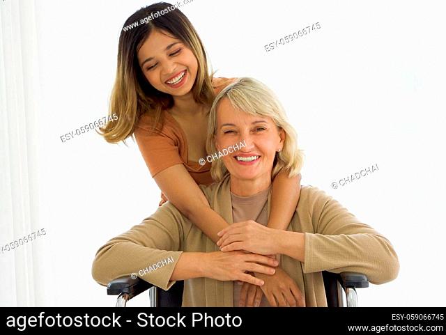 Happy mix skin family living together, adopted asian daughter cuddle caucasian mother sitting on a wheelchair with smiles. Close up