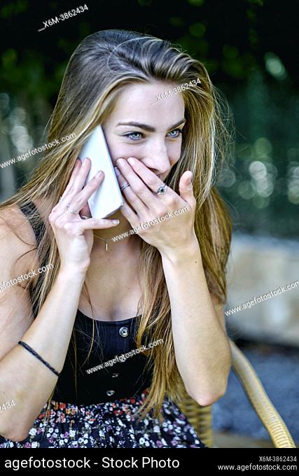 Natural beauty portrait of young woman in her 20s with long hair and blue eyes outdoor in a garden talking on her mobile phone. Lifestyle concept