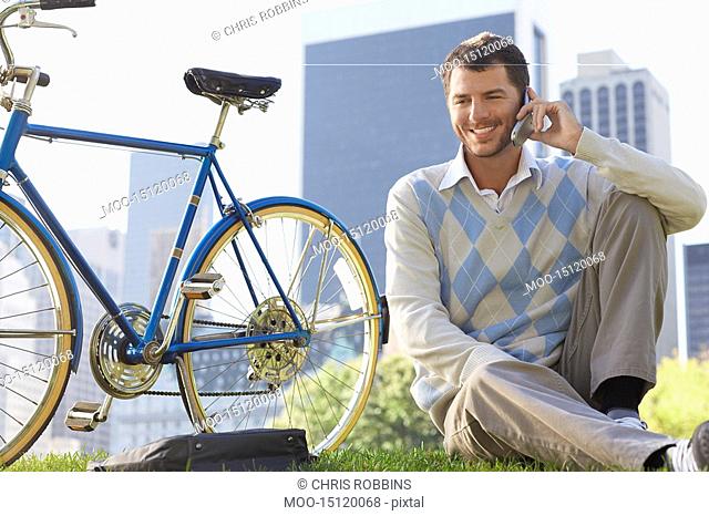 Man sitting on lawn in park talking on mobile phone