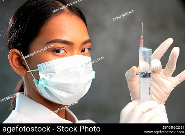 Closeup of young female doctor with syringe. Woman physician in protective mask portrait over concrete wall background