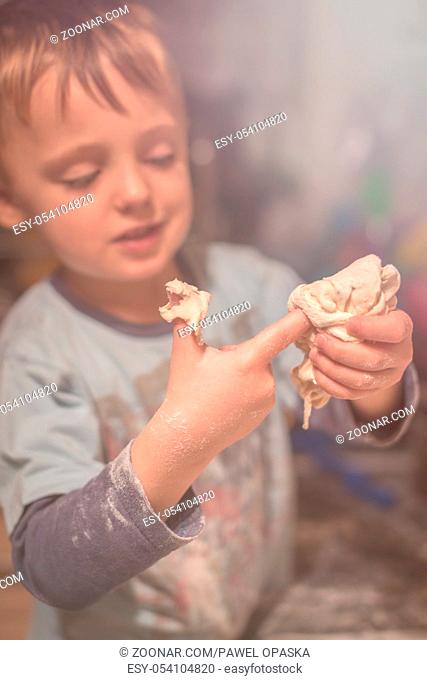 Cute little caucasian boy playing with a dough while helping his mother to prepare traditional polish christmas dish called pierogi
