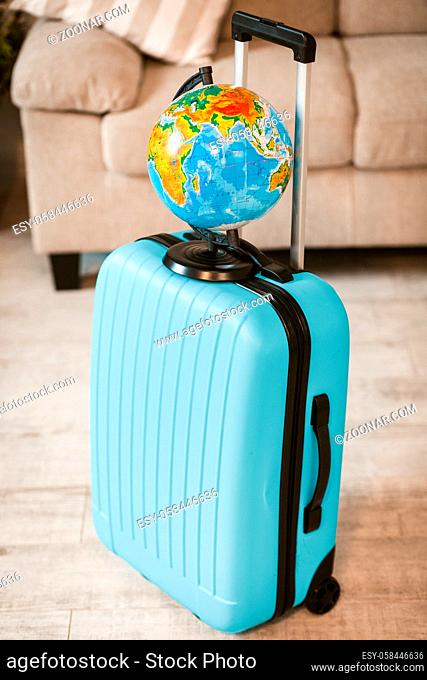 Close up view of bright suitcase with globe. Travel large suitcase standing on floor