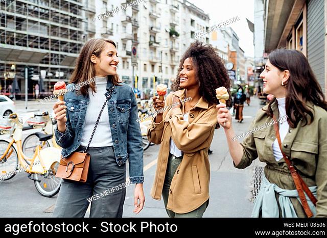 Smiling friends having ice cream while walking at city street