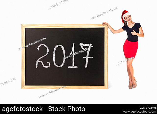 Young business woman in xmas hat stands near big chalkboard with new year date