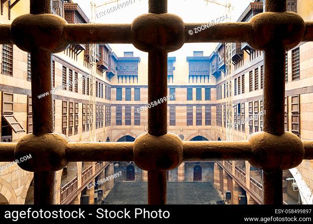 View of the courtyard of caravansary (Wikala) of al-Ghuri through window with iron ornate grid, showing vaulted arcades and interleaved wooden grids...
