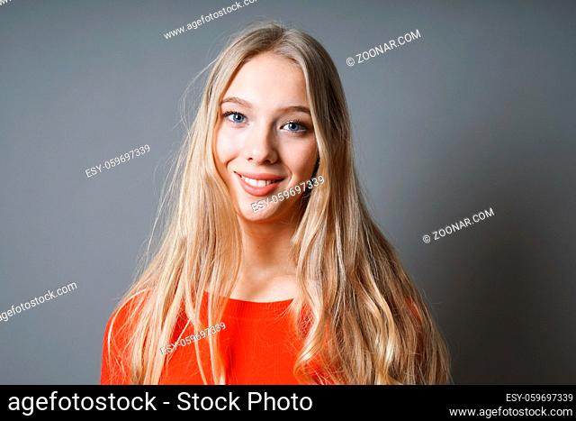 happy young woman with long blond hair and radiant smile against gray background with copy space