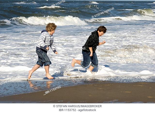 2 boys surprised by a wave on the North Sea coast of Holme Land, Jutland, Denmark, Europe