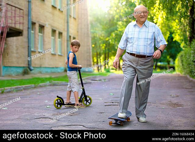 Grandfather and grandson on a walk. A child is watching his grandfather ride on a skateboard
