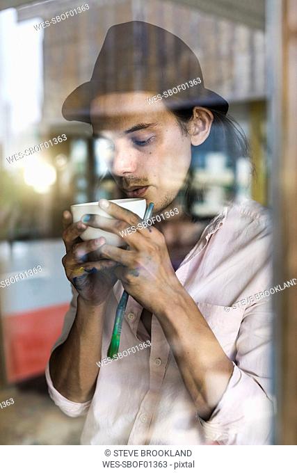 Artist taking a break from his work, leaning agains window, drinking coffee