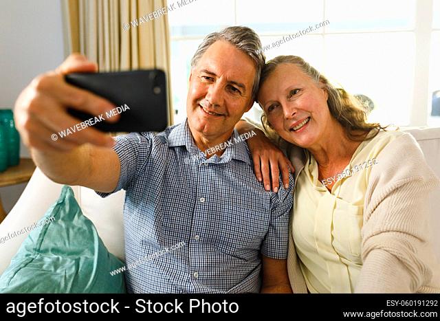 Happy senior caucasian couple in living room, sitting on sofa, taking selfies and smiling
