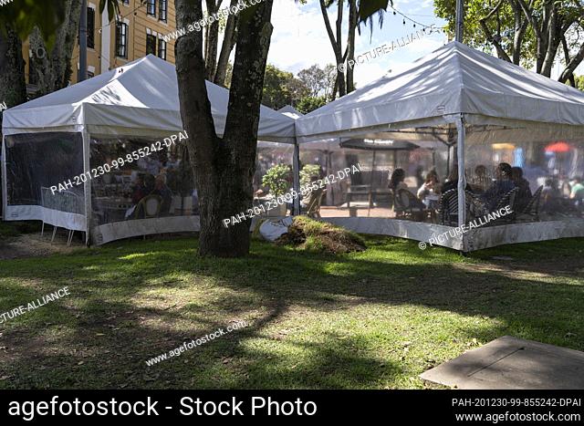 20 December 2020, Colombia, Bogotá: Customers sit in pavilions set up next to a restaurant in a park in Bogota. Several restaurants in the city have installed...