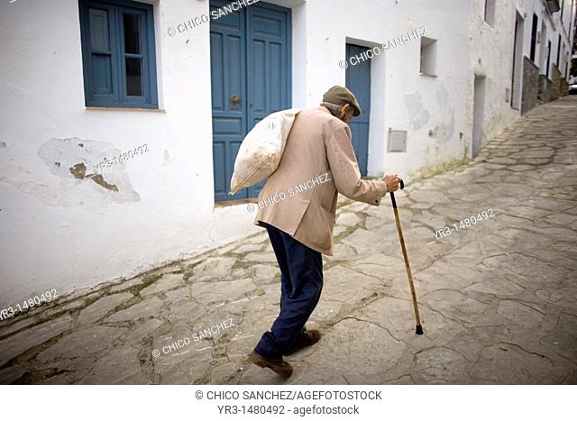 A senior man carrying a bag ups a hill using his walking stick in a street of El Gastor village in the Sierra de Grazalema Natural Park, Cadiz province