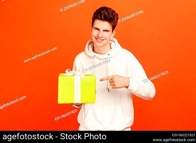 Smiling teenager in casual style sweatshirt pointing finger on big gift box in hand, promotions and discounts in your tariff, mobile communications