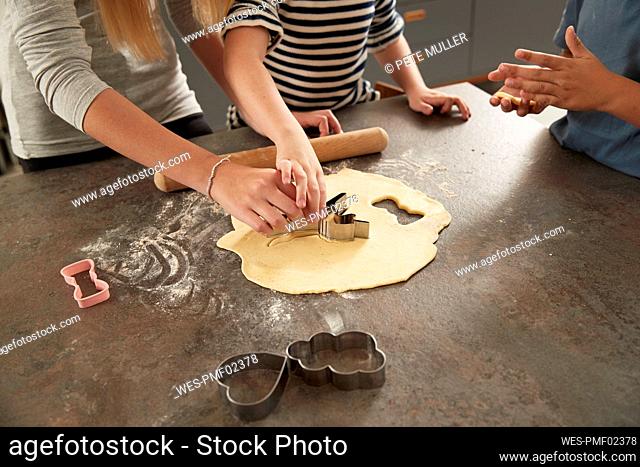 Hands of children using cookie cutter at kitchen counter