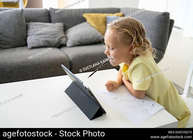 Girl with pencil in mouth leaning on table at home